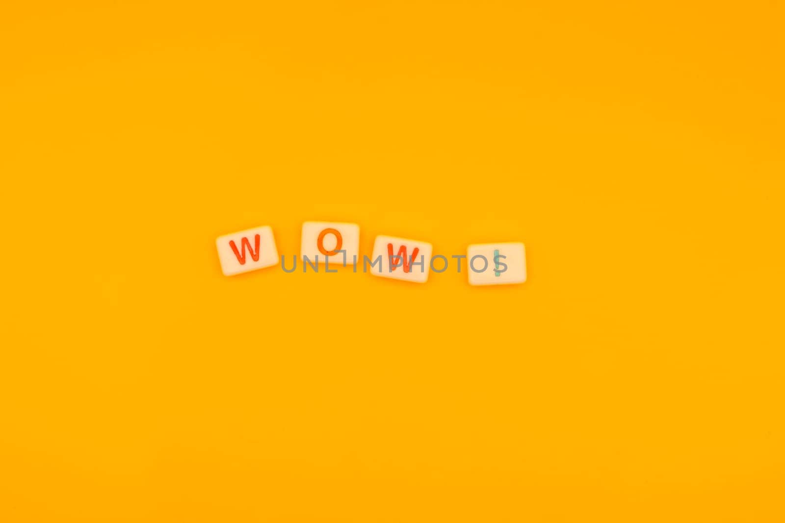 Close-up of Scrabble tiles spelling WOW arranged on a vibrant yellow background, minimalistic style with copy space for creative designs.
