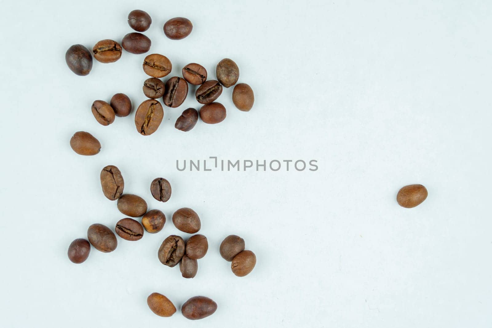 A scattered group of roasted coffee beans placed randomly on a clean white background, showcasing a minimalistic and natural arrangement.