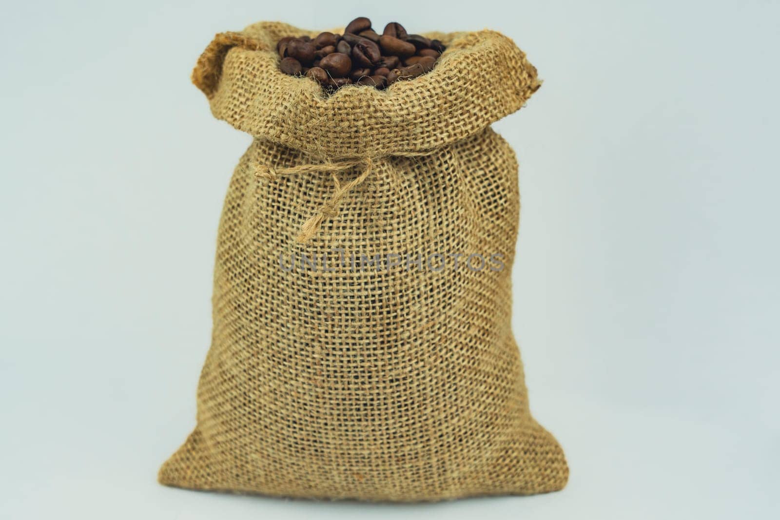 A burlap sack tightly filled with roasted coffee beans, standing upright on a white background, showcasing rustic packaging and texture.