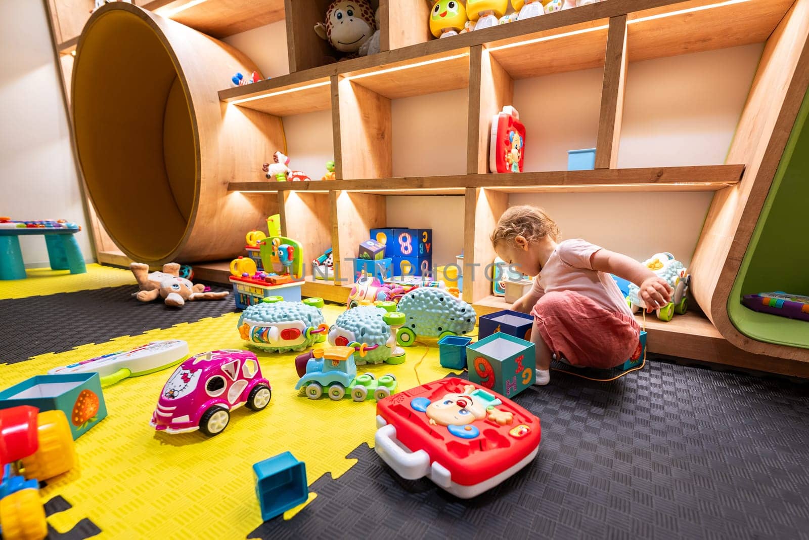 A child focused on exploring and playing with various toys in a bright and organized modern playroom. Concept of fun and interactive learning