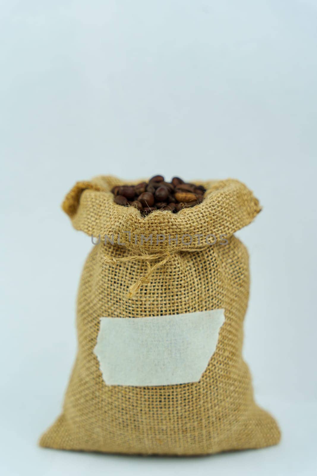 Burlap sack tightly filled with roasted coffee beans, featuring a blank label for customization, standing upright on a white background.