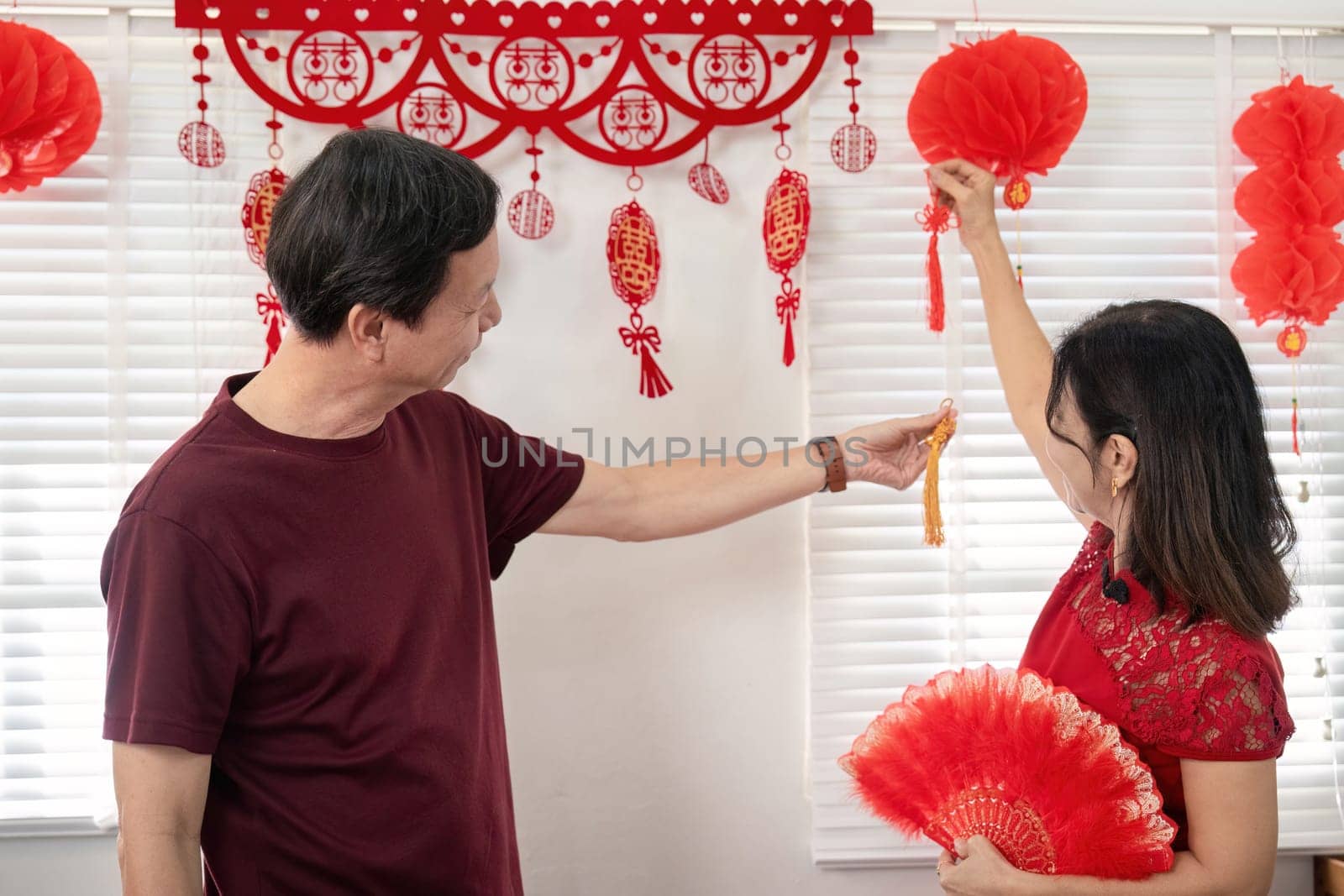 An elderly Chinese couple joyfully celebrates Chinese New Year at home surrounded by festive decorations and traditions.