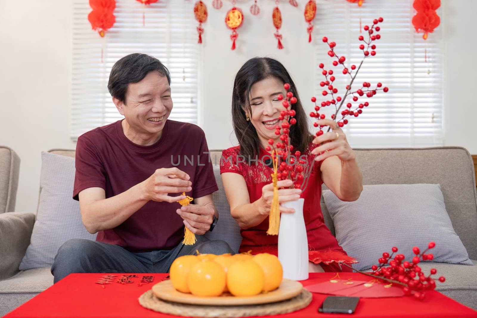 An elderly Chinese couple joyfully prepares for Chinese New Year surrounded by vibrant decorations and traditional symbols of good fortune.