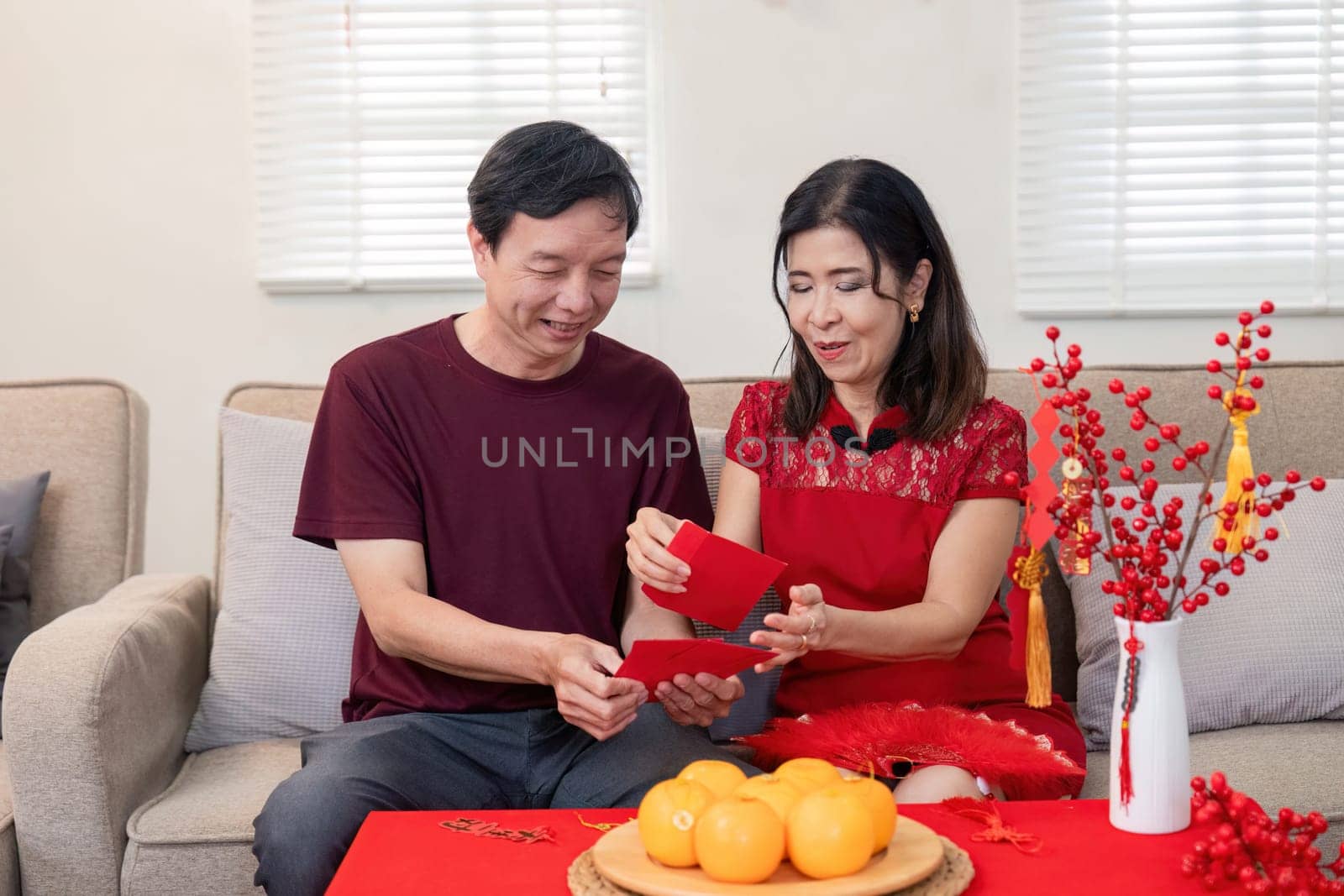 A joyful elderly Chinese couple exchanges red envelopes embodying the spirit of Chinese New Year in a cozy home environment.