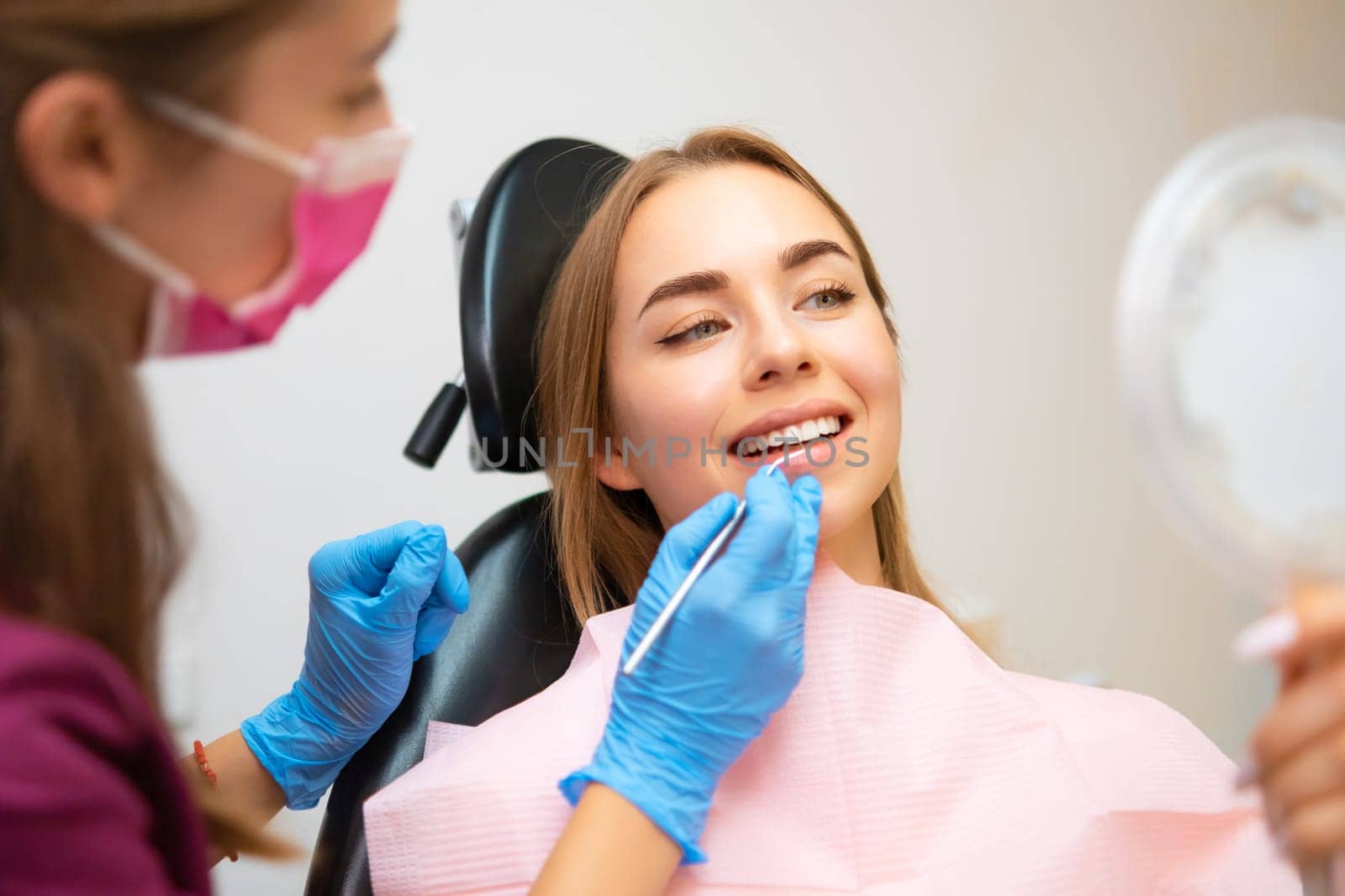 Woman patient sitting in armchair during dental treatment in dental clinic. Doctor checking front teeth with instrument to check soundness of teeth