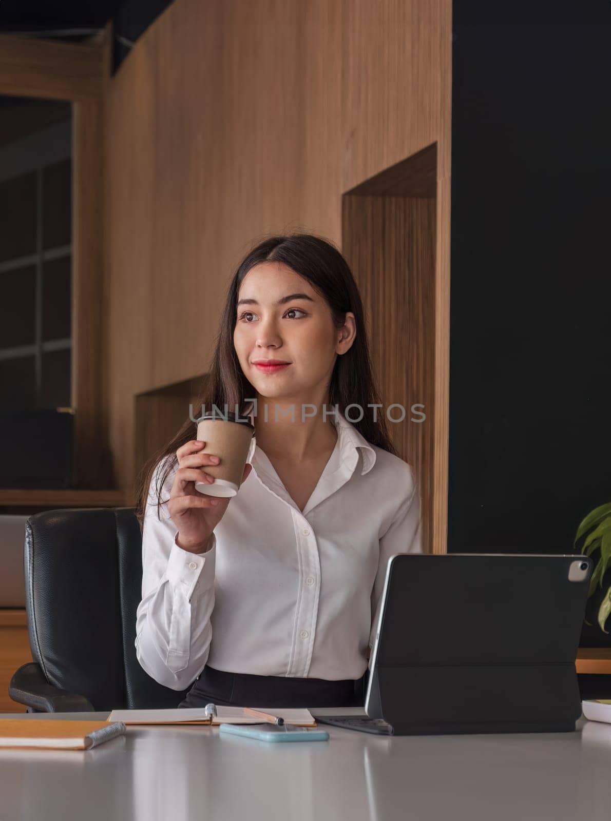 Asian businesswoman drinking coffee with tablet on desk at office. by wichayada