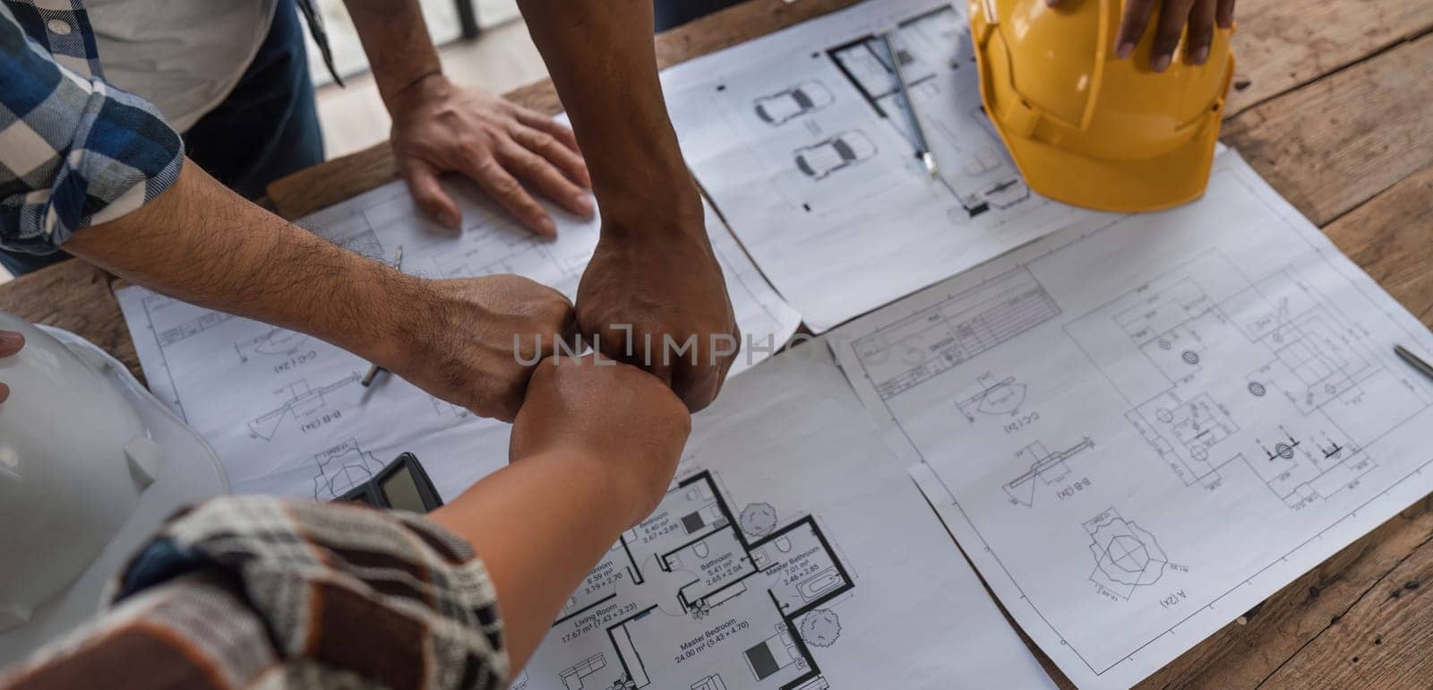 A team of engineers who successfully planned work on a modern home construction project shook hands and congratulated the team on their success. by wichayada