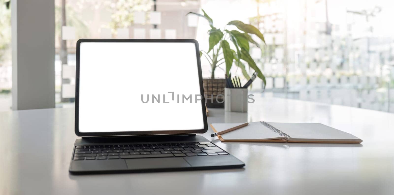 laptop white screen mockup, painting tools, notebook, and decor on a table in a modern contemporary living room. close-up workspace..