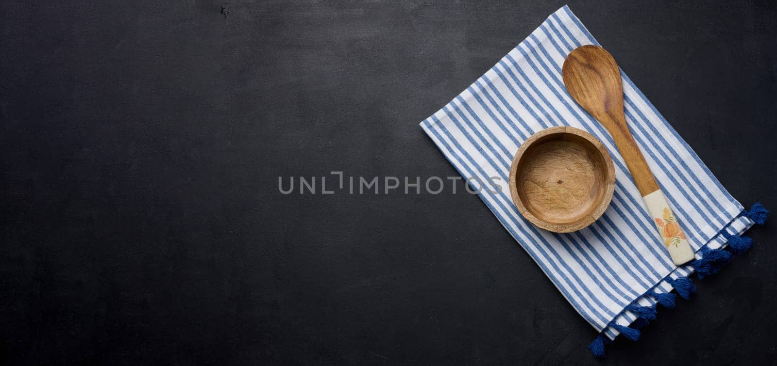 Empty bowl and wooden spoon on a black table, top view. Copy space