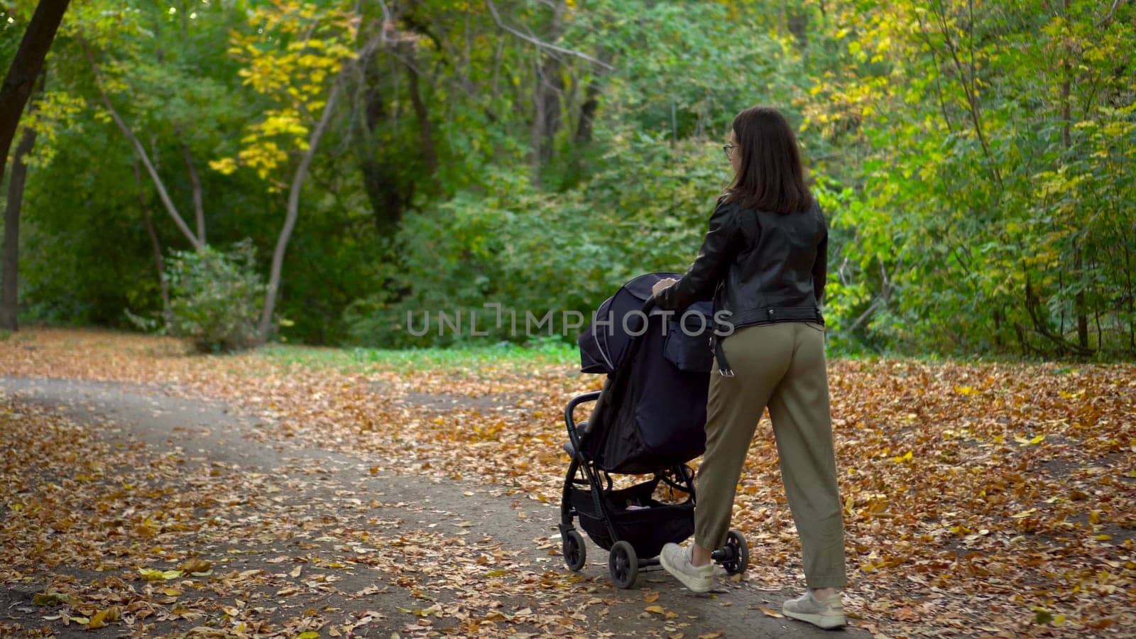 A young mother walks through the forest with a sleeping child in a stroller. A woman with glasses walks in an autumn park. 4k