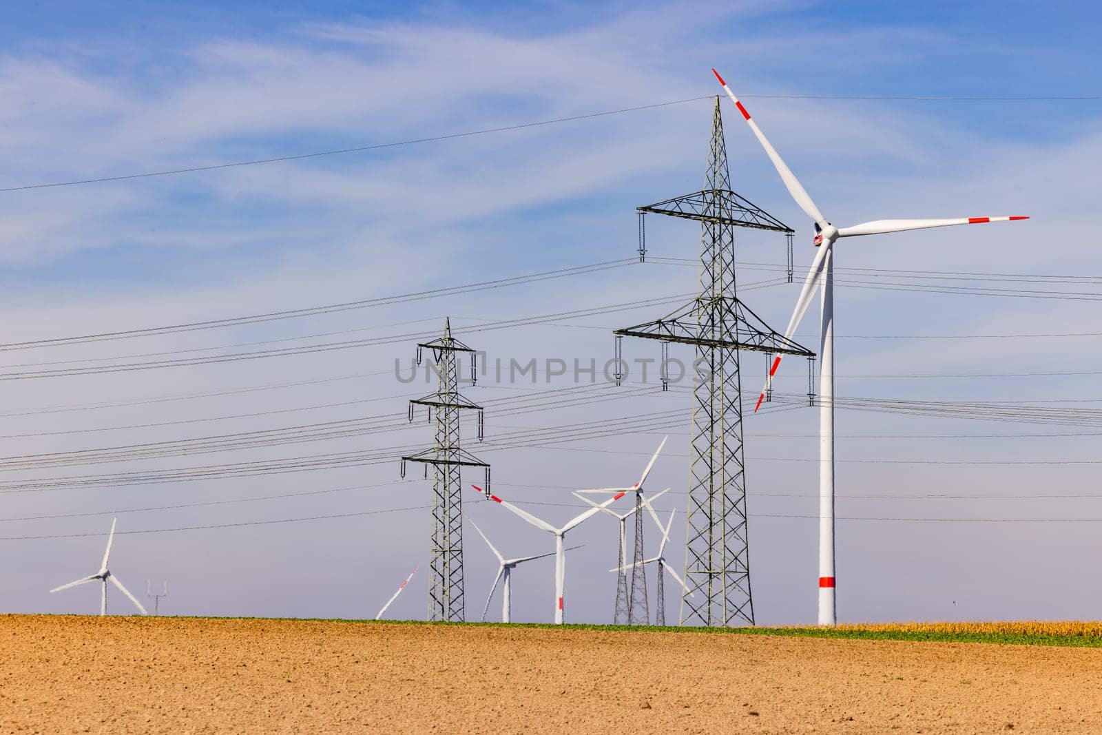 Field with many wind turbines of a wind turbine and power lines of several power poles under blue sky