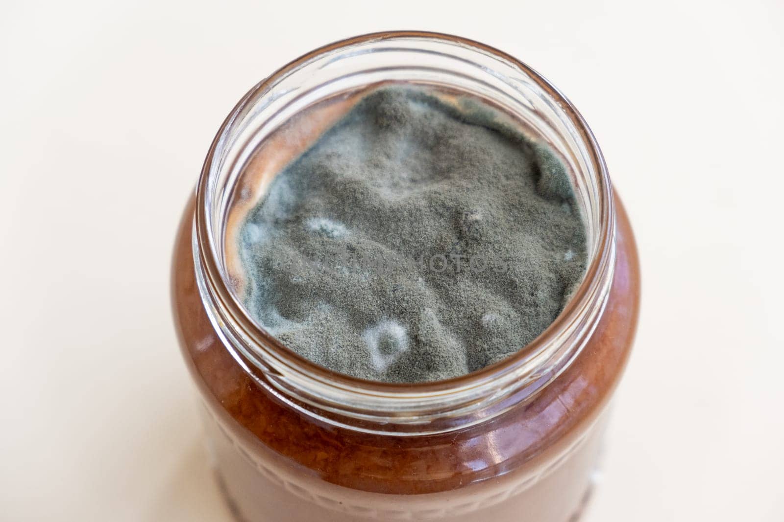 Open jar with sweet jam and mold on a white background. Mold in a jar of raspberry jam. Hazardous to health.