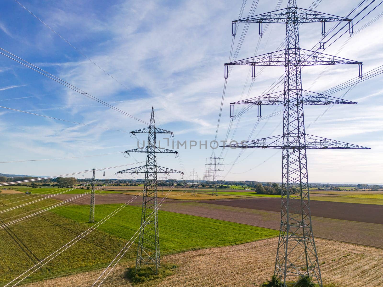 Aerial view of a row of high voltage pylons with many power lines in rural area to the horizon