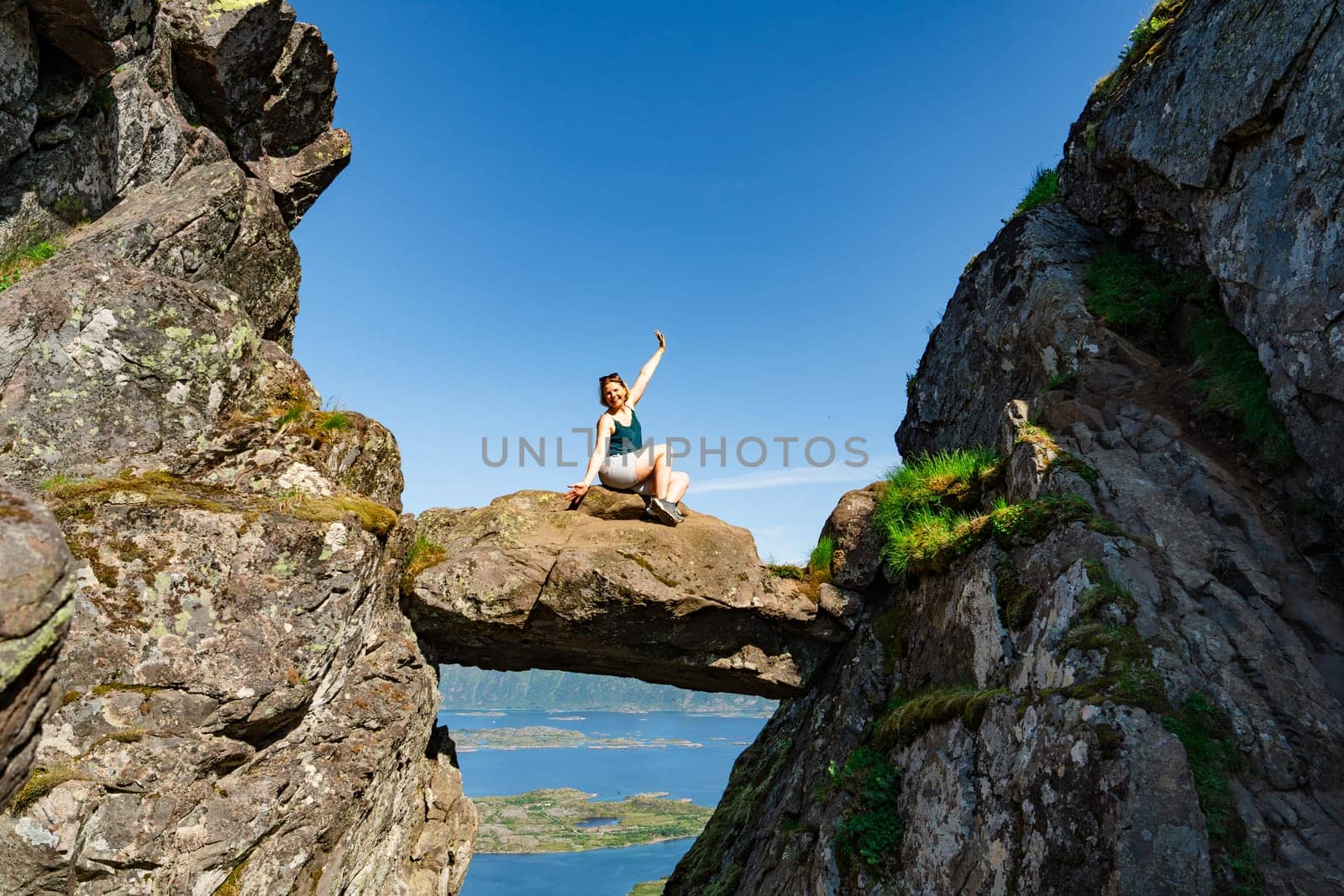 Brave traveler woman standing on hanging stone between rocks. Djevelporten in Norway Lofoten islands by PhotoTime