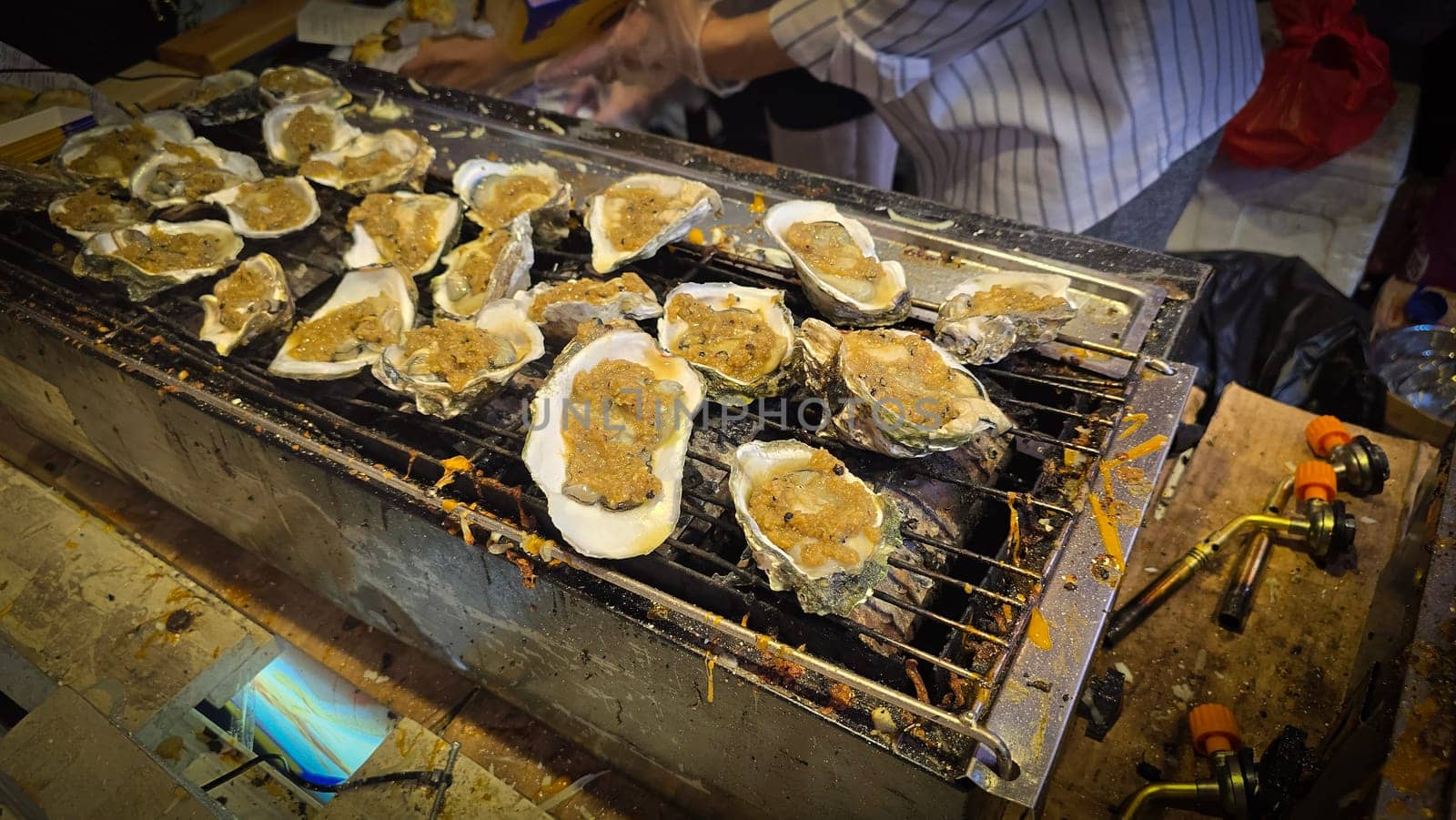 street vendor uses a torch flame to prepare delicious grilled oyster with flair and skill, showcasing the vibrant atmosphere of bustling night Thai markets. Good for recipe book