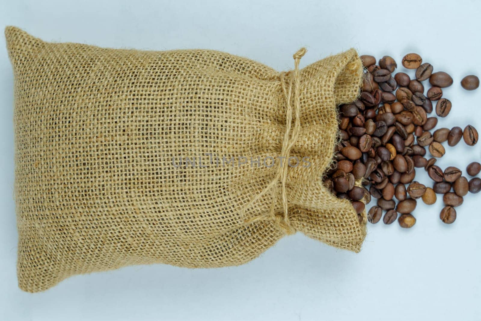 Overhead view of a burlap sack with roasted coffee beans spilling onto a white surface, highlighting natural material and coffee texture.