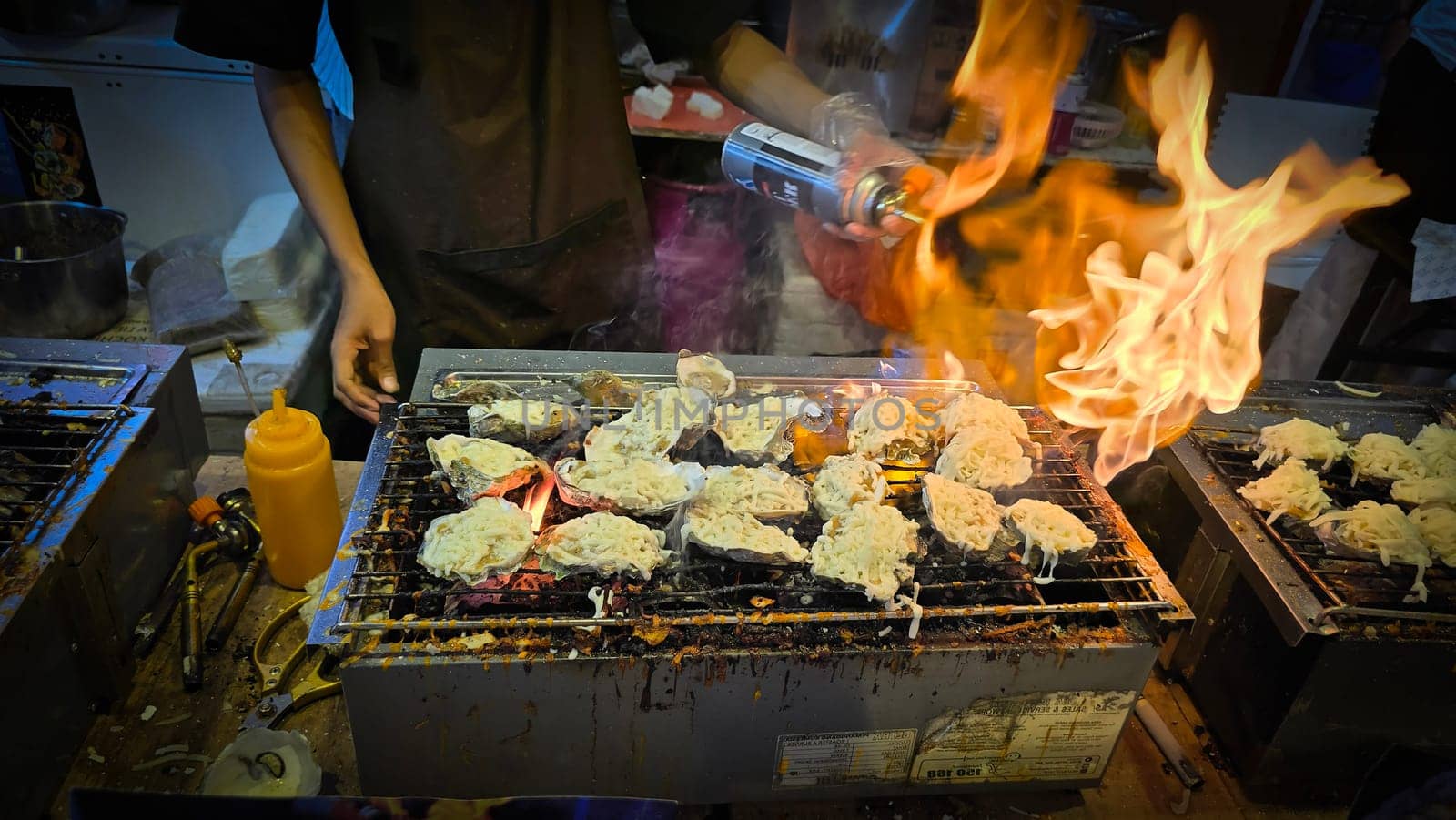 street vendor uses a torch flame to prepare delicious grilled oyster with flair and skill, showcasing the vibrant atmosphere of bustling night Thai markets. Good for recipe book