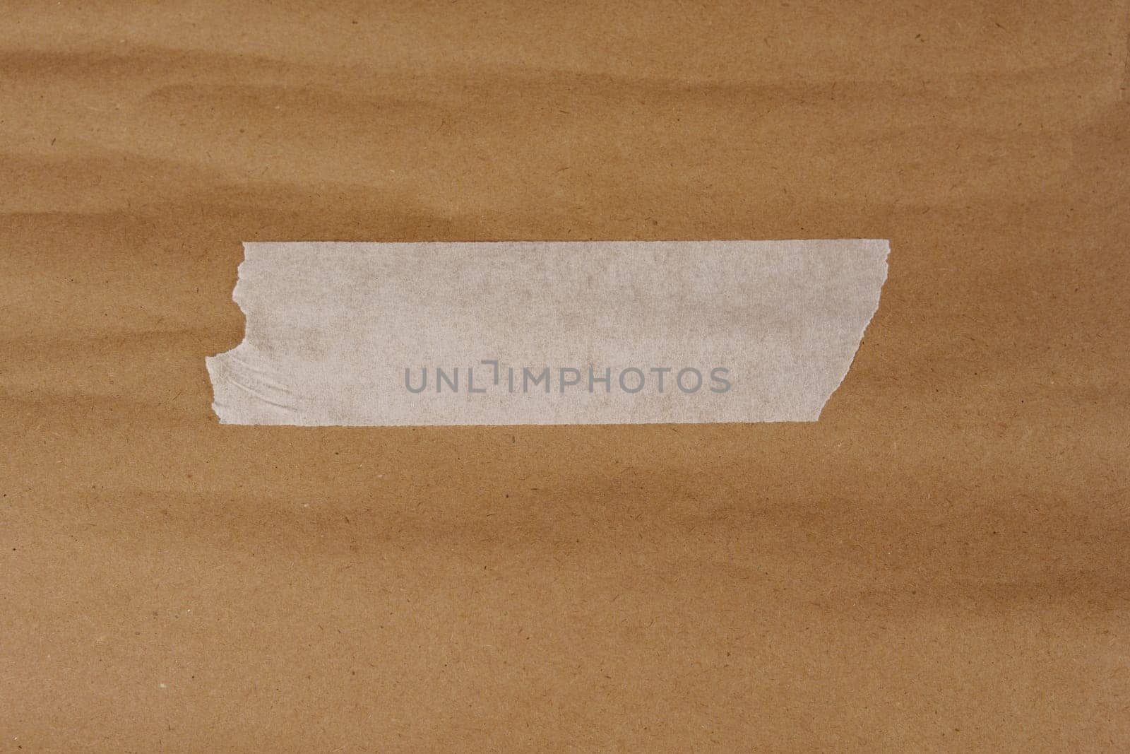 A piece of torn white adhesive tape placed on a textured brown kraft paper surface, suitable for design, scrapbooking, and creative projects.