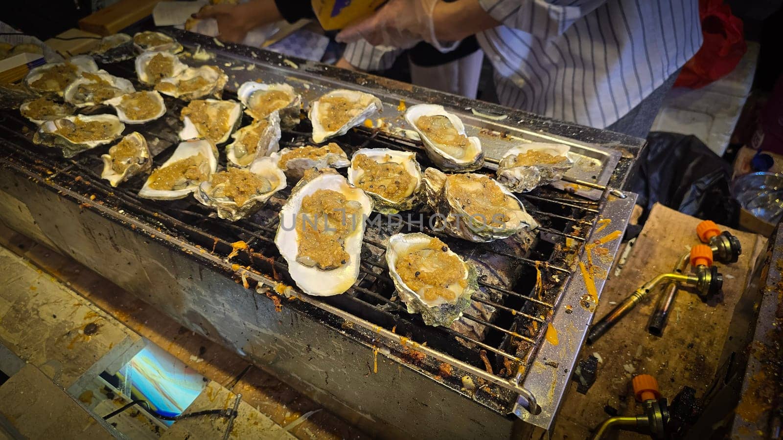 street vendor uses a torch flame to prepare delicious grilled oyster with flair and skill, showcasing the vibrant atmosphere of bustling night Thai markets. Good for recipe book