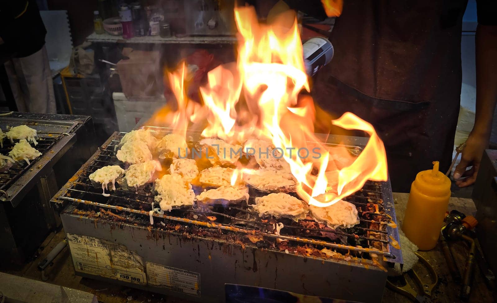 street vendor uses a torch flame to prepare delicious grilled oyster with flair and skill, showcasing the vibrant atmosphere of bustling night Thai markets. Good for recipe book