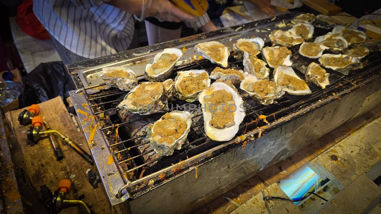street vendor uses a torch flame to prepare delicious grilled oyster with flair and skill, showcasing the vibrant atmosphere of bustling night Thai markets. Good for recipe book