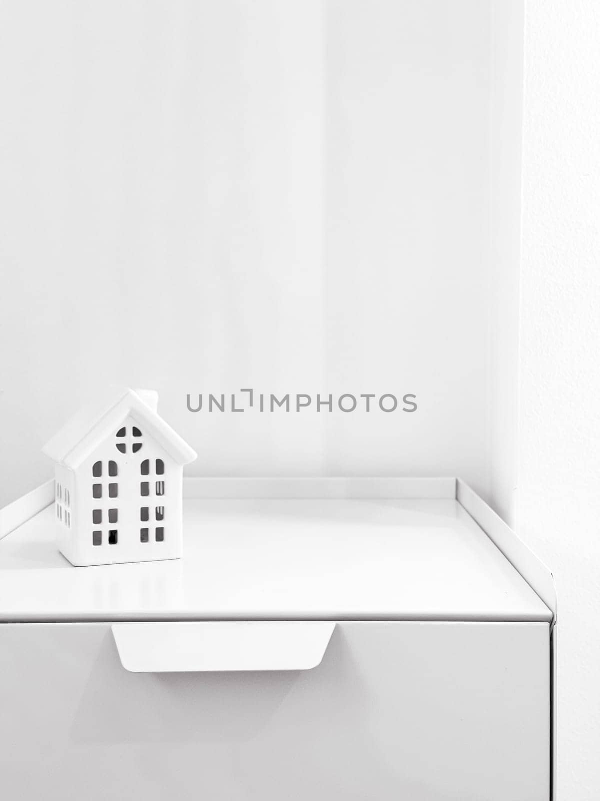 Minimalist white house model on a white shelf with bright lighting.