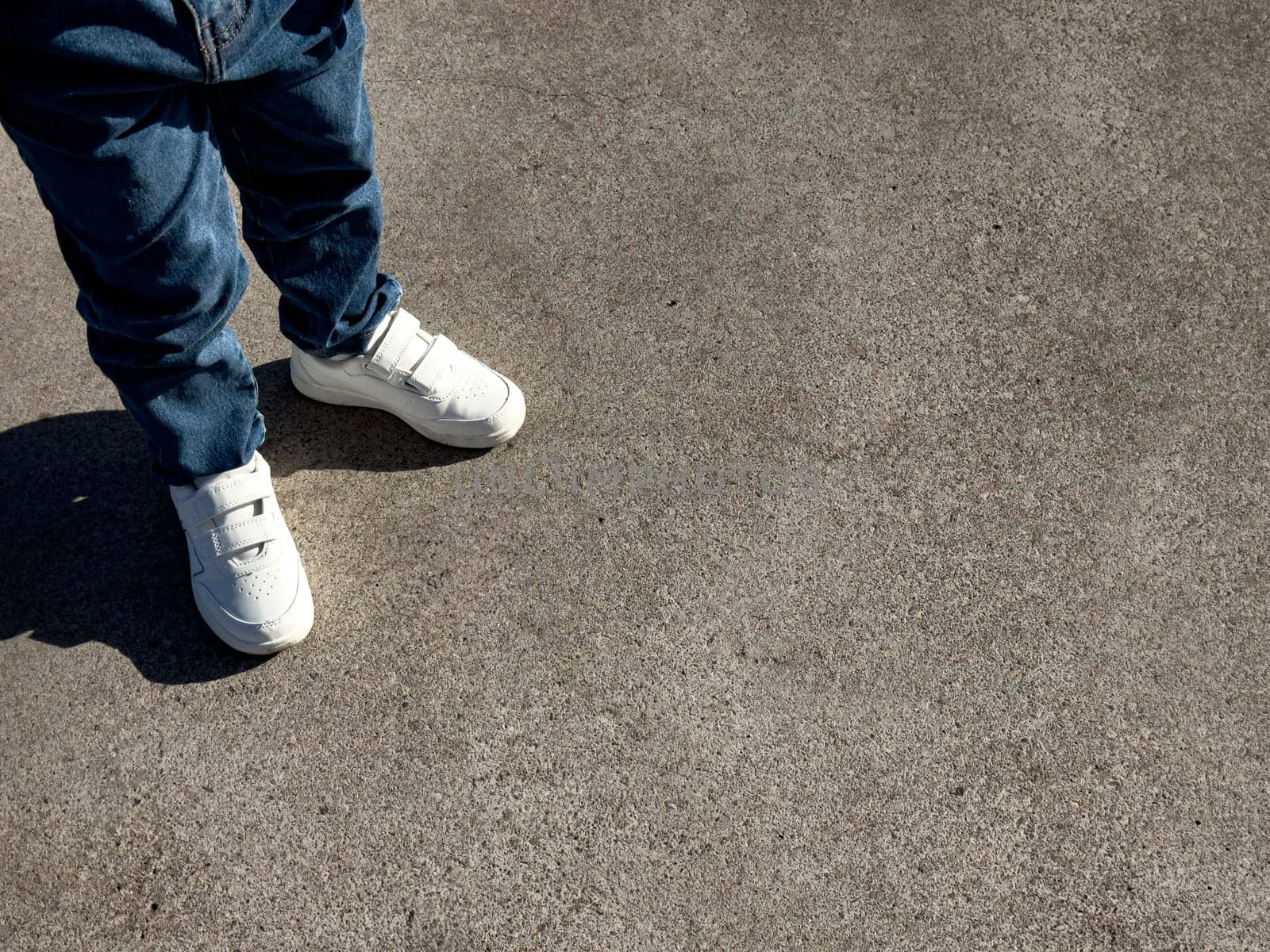 Young child wearing white sneakers on concrete surface.