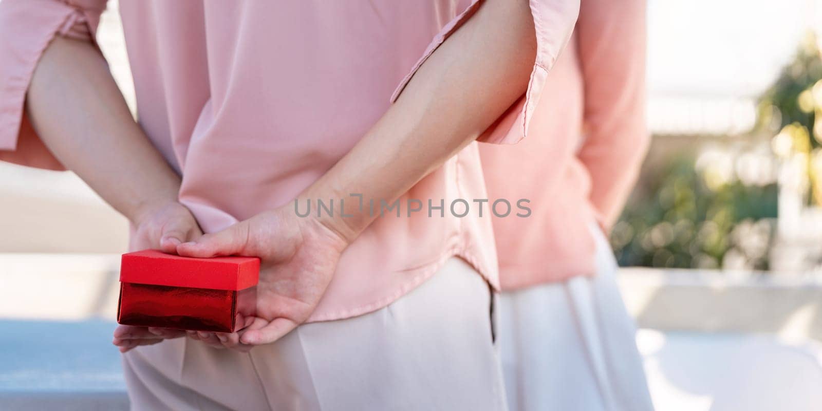 A couple shares a heartfelt Valentine moment as one surprises the other with a special gift capturing love in a beautiful setting.