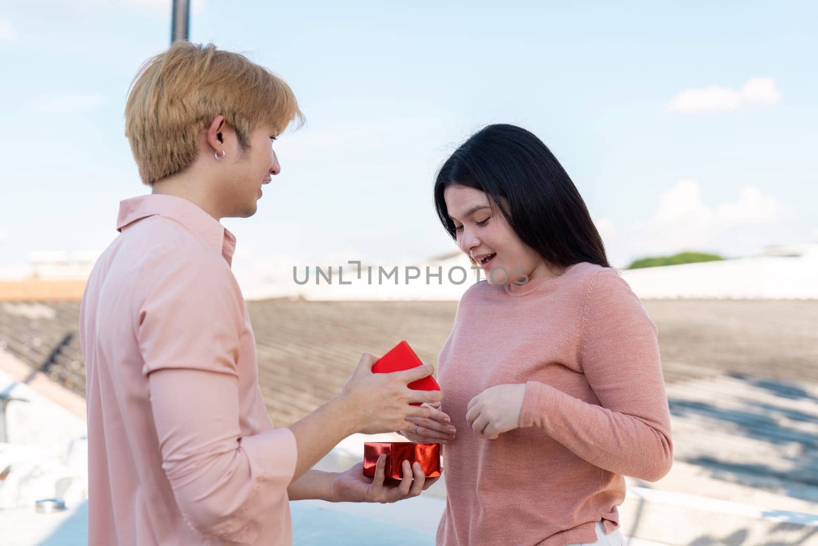 A couple shares a heartfelt moment on a rooftop exchanging Valentine gifts filled with love.