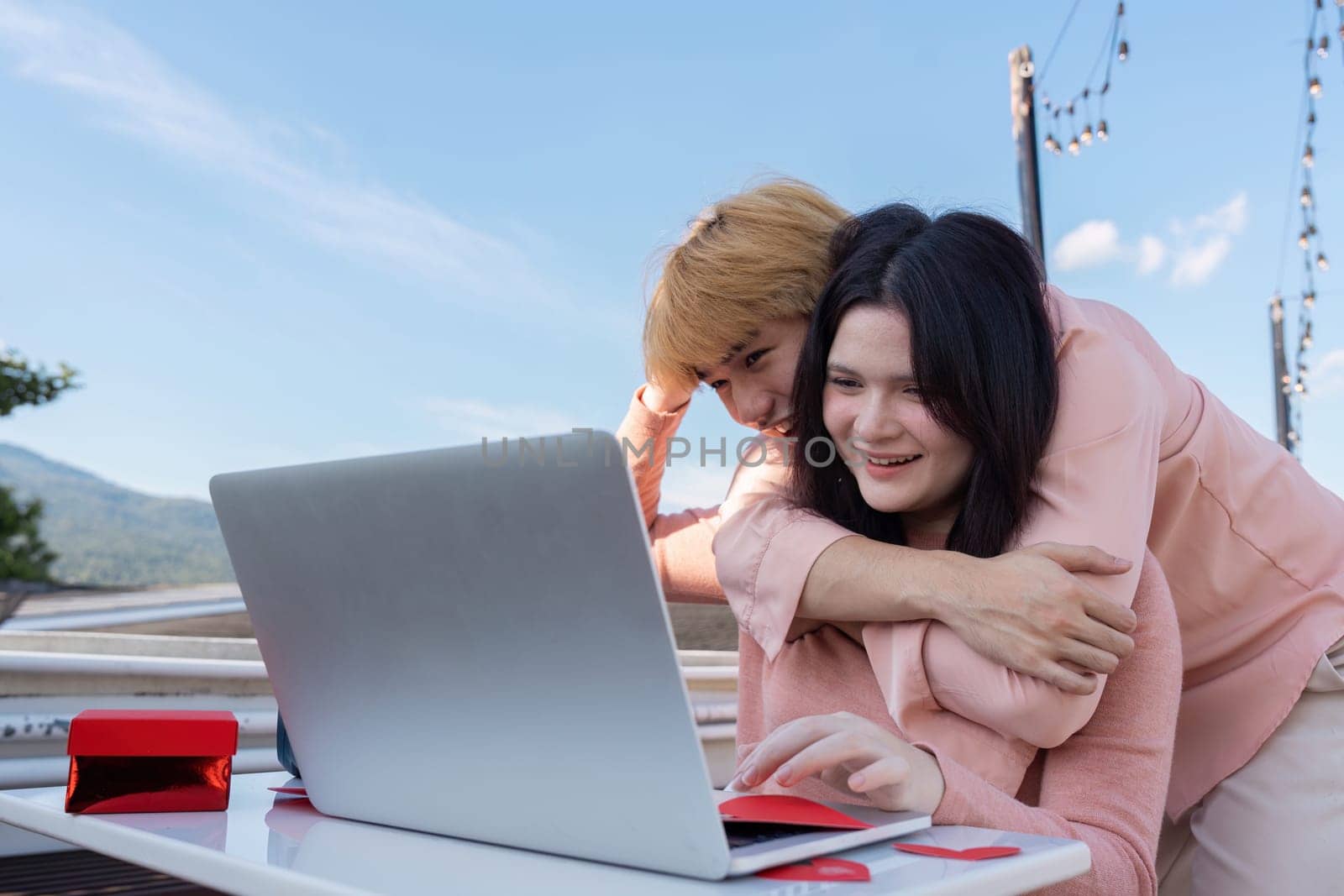 A couple enjoys a cozy moment outdoors sharing laughter over a laptop surrounded by a beautiful scenic view in a romantic atmosphere.