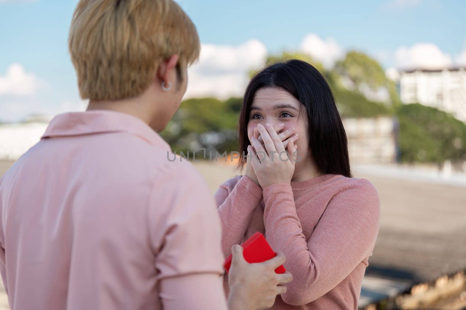 A couple shares a heartfelt moment as one surprises the other with a Valentine proposal outdoors.