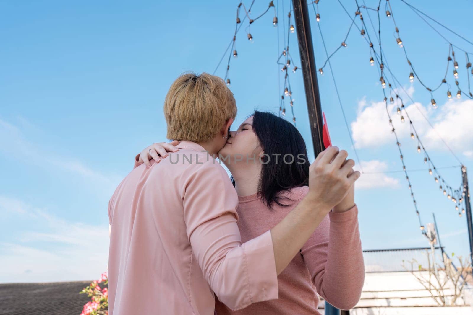 A couple shares a romantic kiss under twinkling lights on a rooftop celebrating love on Valentine Day.