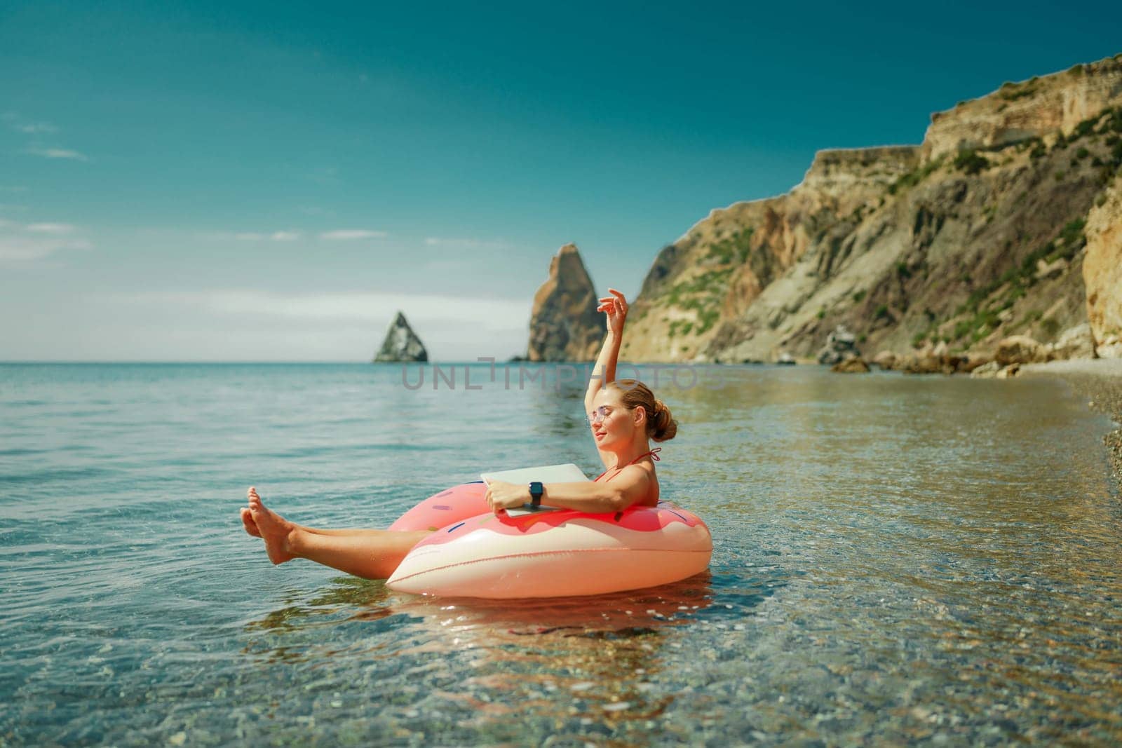 Woman laptop sea. Freelancer woman in sunglases floating on an inflatable big pink donut with a laptop in the sea. People summer vacation rest lifestyle concept