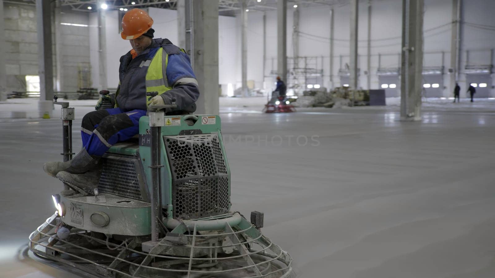 A skilled worker operates a concrete finishing machine to smooth a floor in a large industrial space. Clip