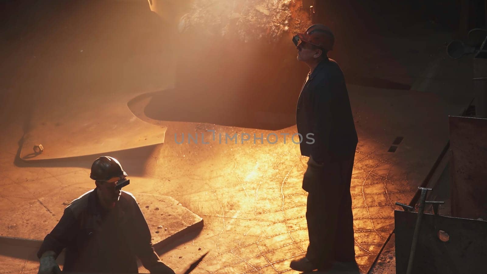 A skilled metalworker oversees molten metal pouring in a busy factory, showcasing industry and craftsmanship. Stock Clip