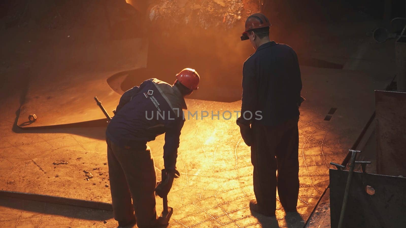 A skilled metalworker oversees molten metal pouring in a busy factory, showcasing industry and craftsmanship. Stock Clip