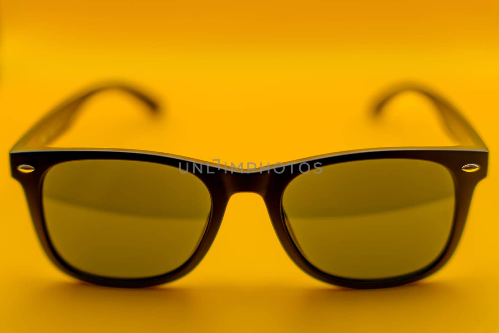 Close-up of stylish black-framed sunglasses with green-tinted lenses, photographed against a vibrant yellow background.