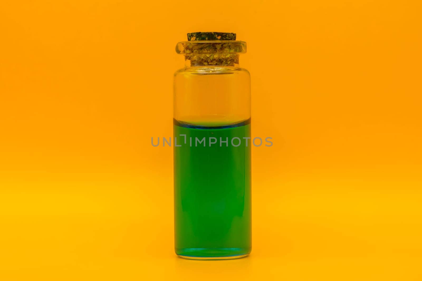 Close-up of a small corked glass bottle containing vibrant green liquid, isolated against a bright yellow background.