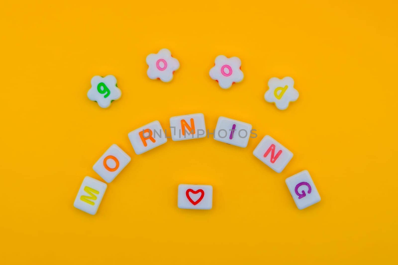 Cheerful "Good morning" spelled out with vibrant letters in a creative arc on a bright yellow background, featuring a heart symbol for positivity.