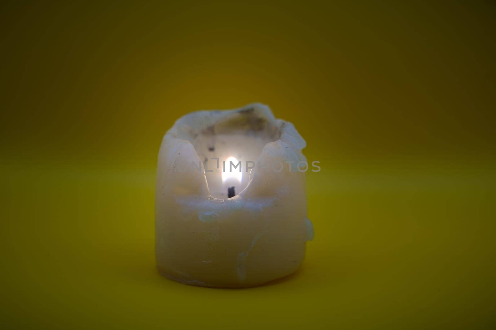 A melting wax candle with a burning flame, displayed against a vibrant yellow background, symbolizing warmth, light, and simplicity.