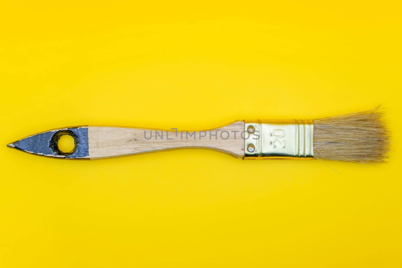Flat lay of a wooden paintbrush with natural bristles and a metallic ferrule, isolated against a bright yellow background.