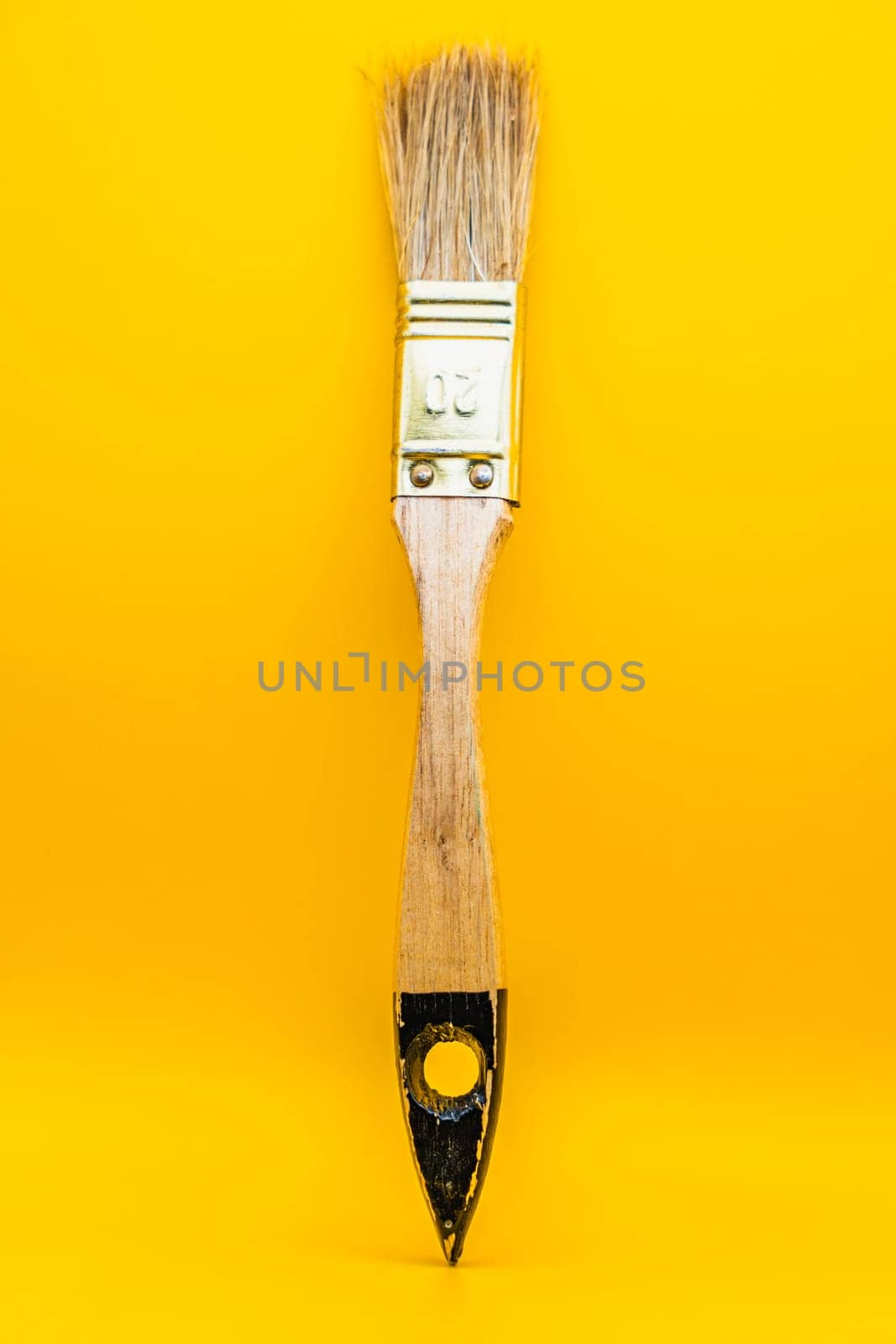 Close-up of a wooden paintbrush with natural bristles and a metallic ferrule, isolated against a bright yellow background.