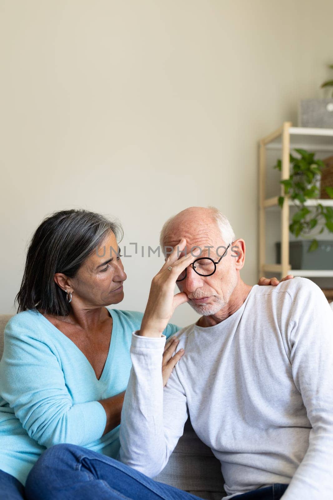 Vertical portrait of mature woman comforting sad man sitting on the couch at home living room. Copy space. Mental health concept.