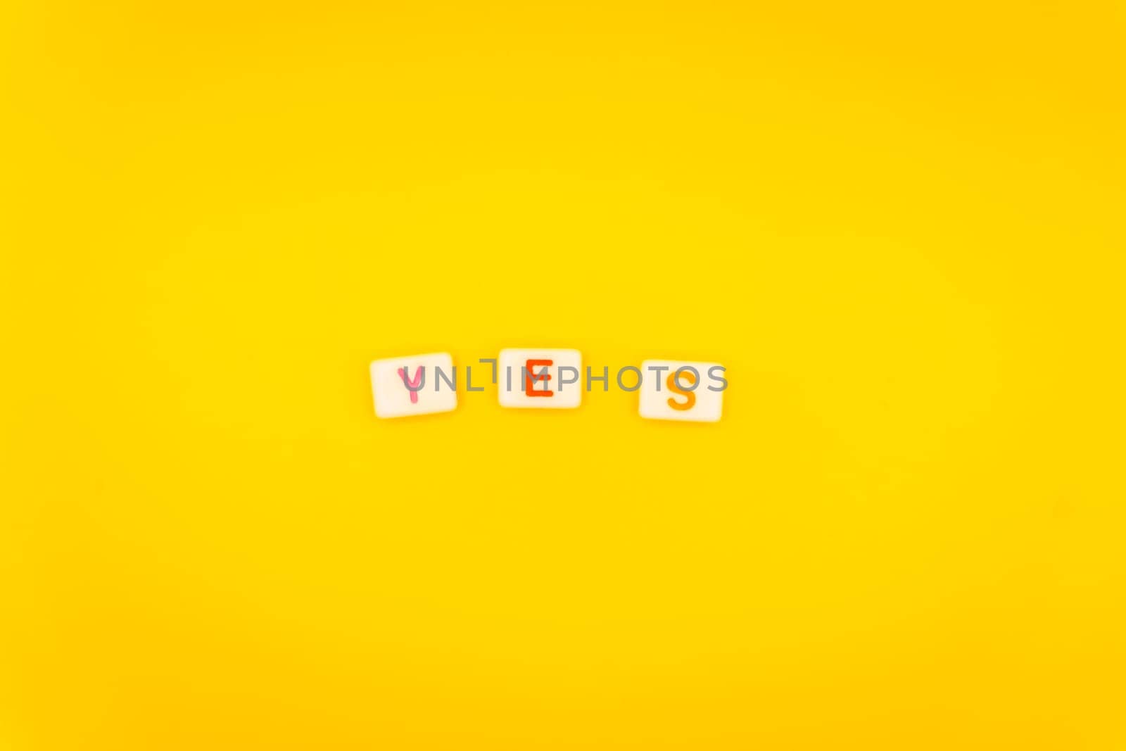 Minimalist arrangement of alphabet tiles spelling "Yes" with colorful letters on a bright yellow background, symbolizing affirmation and positivity.