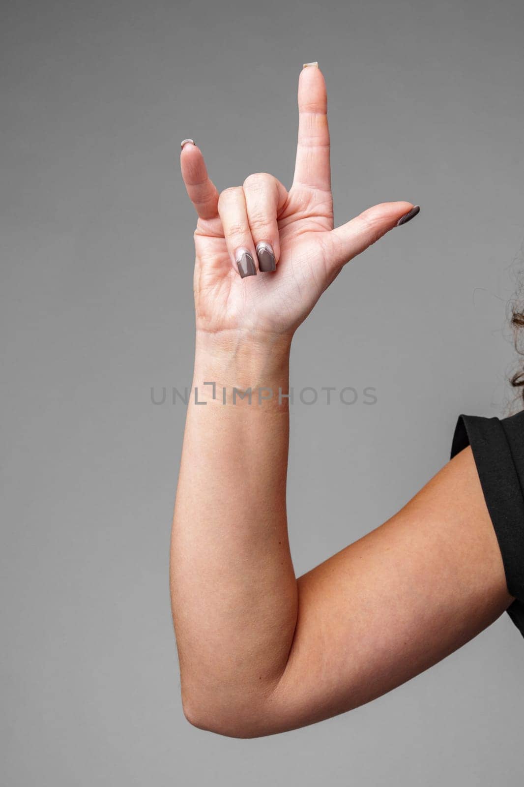 A person making the I love you gesture with their hand in front of a neutral gray background close up