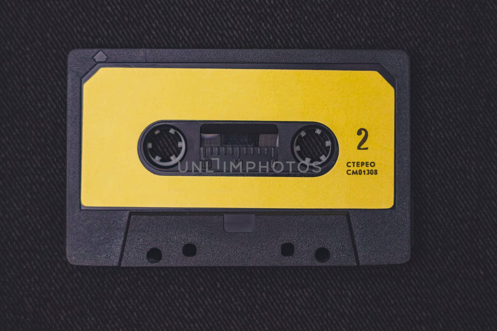 A vintage audio cassette tape in black with a yellow label, featuring stereo marking, captured on a textured dark background for a nostalgic aesthetic.