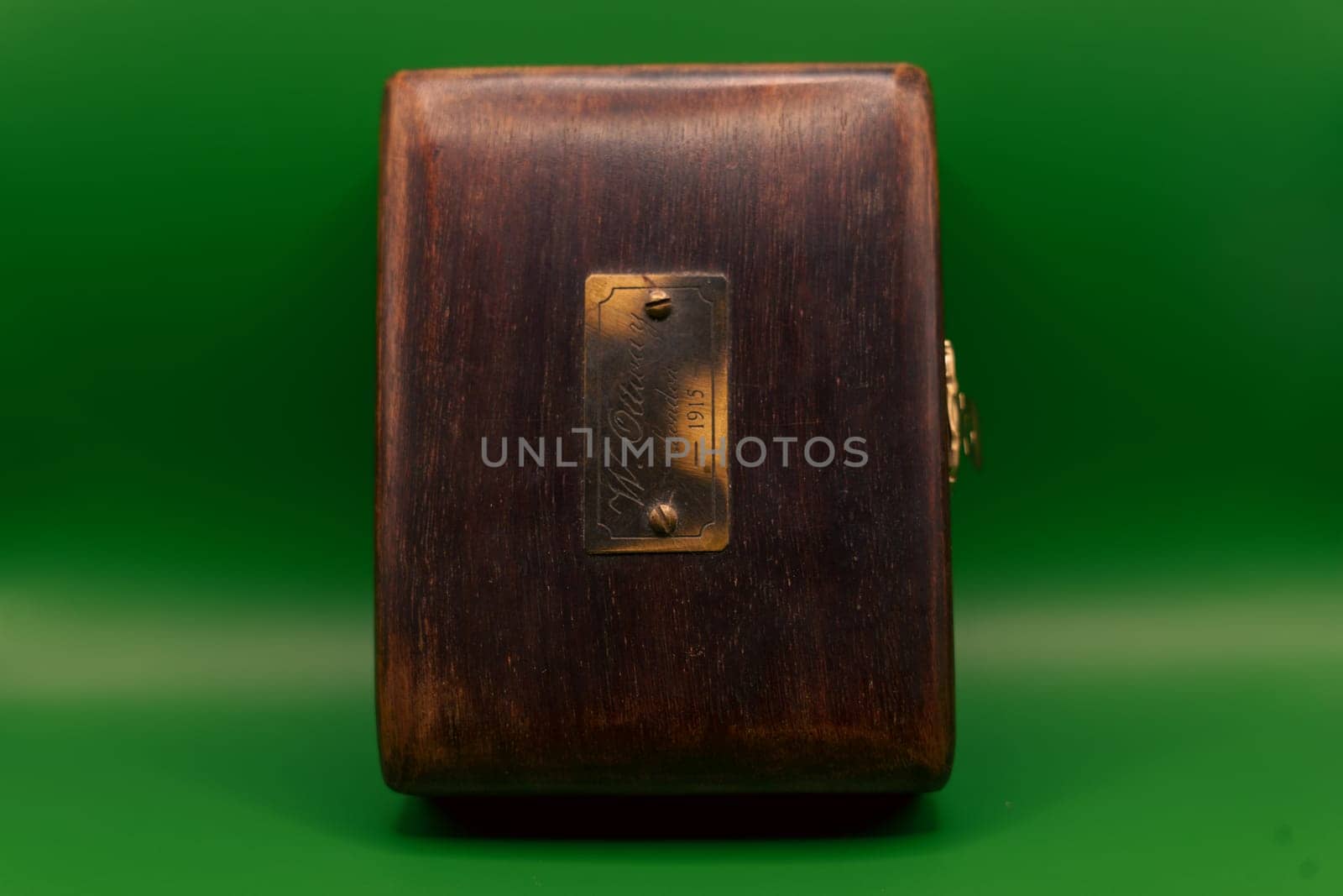 A vintage wooden box featuring a brass nameplate engraved with "W. Ottaway, London, 1915," set against a vibrant green background.