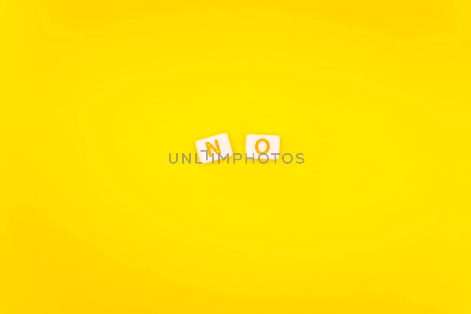 Minimalist arrangement of alphabet tiles spelling "No" with colorful letters on a bright yellow background, symbolizing negativity or refusal.
