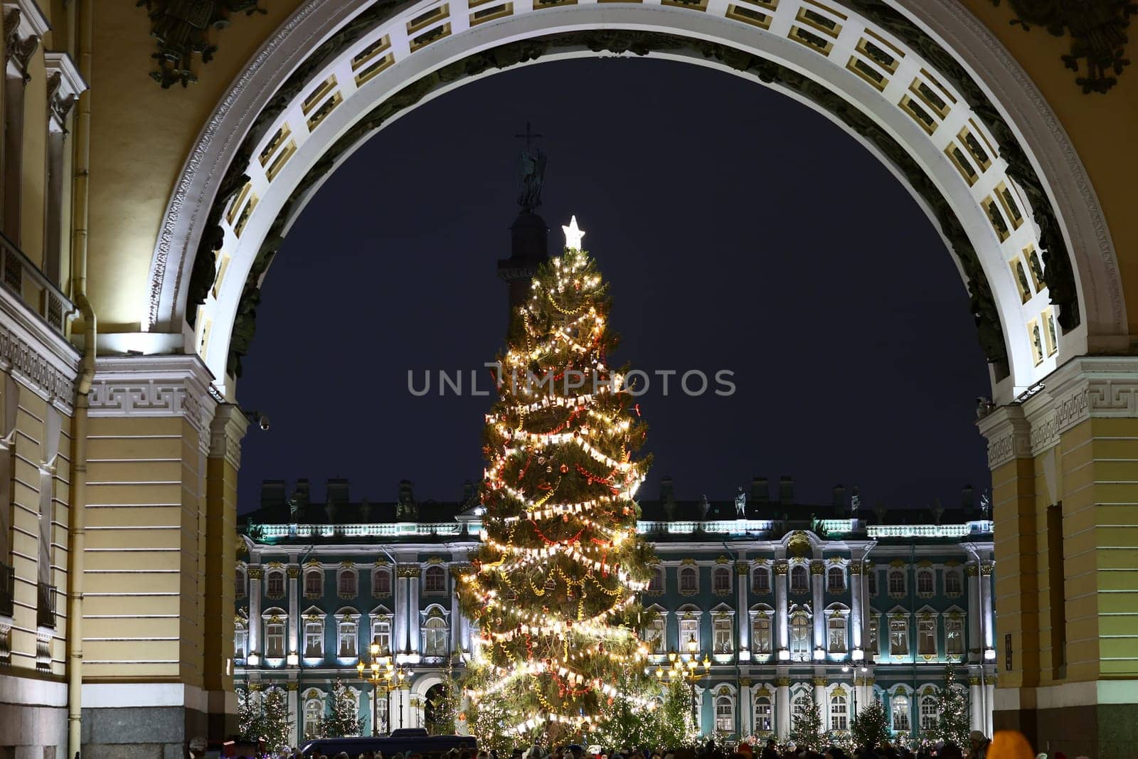 A beautifully lit and adorned Christmas tree stands majestically and gracefully beneath a grand arch at night