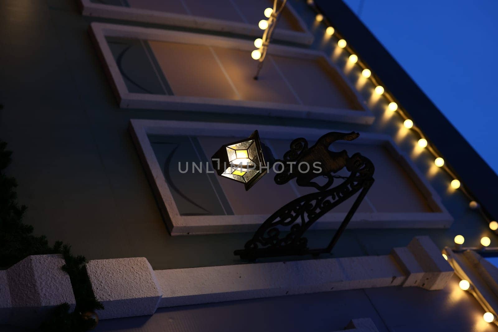 A detailed decorative lantern softly lights a charming building, creating a cozy evening atmosphere